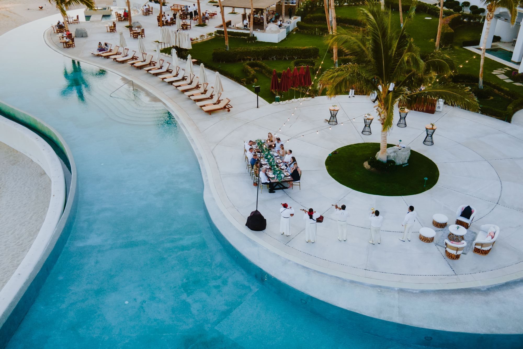 Overhead view of a vibrant poolside event with a long dining table and musicians at Marquis Los Cabos Resort