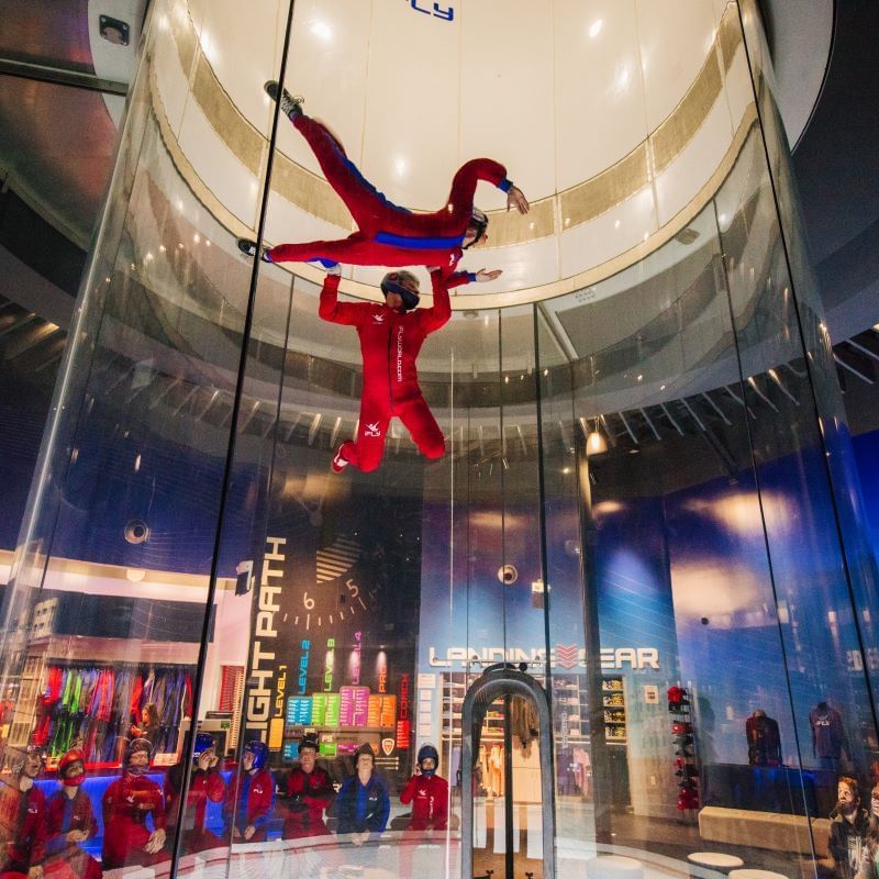 Two people wearing red jumpsuits floating in a tunnel at iFLY Orlando, a fun thing to do within 5 minutes ofRosen Inn at Pointe Orlando.