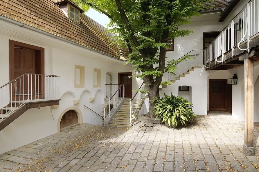 Historic courtyard of the Beethoven Museum in Vienna featuring white façades, stairways, and a leafy tree providing shade