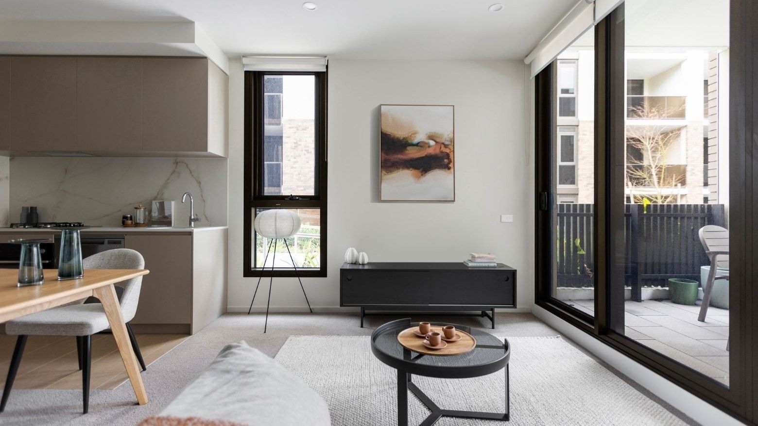 Modern apartment living room with a dining area, sliding glass doors, and a small kitchen.