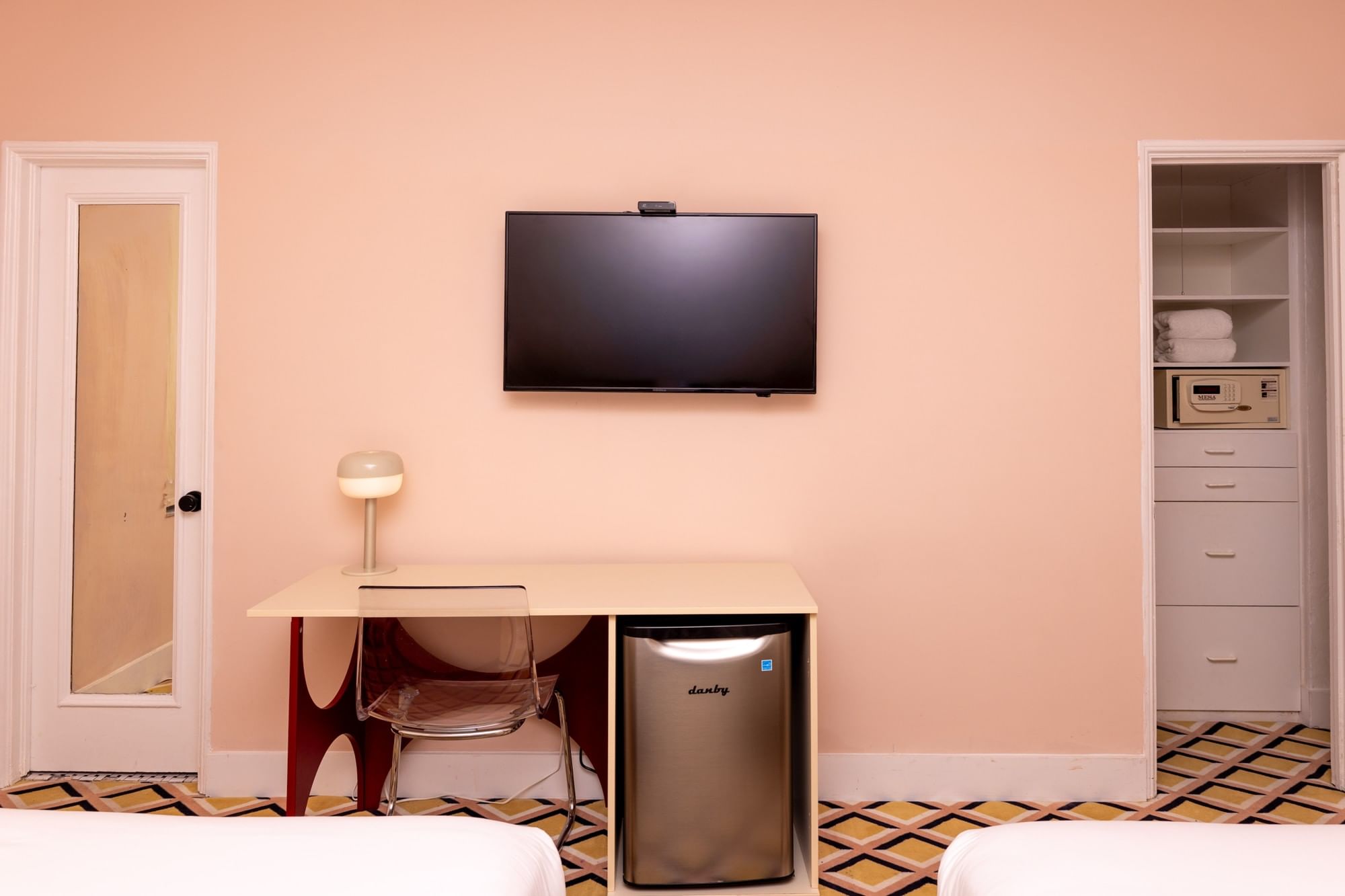 A hotel room with a desk, TV, mini-fridge, and closet.