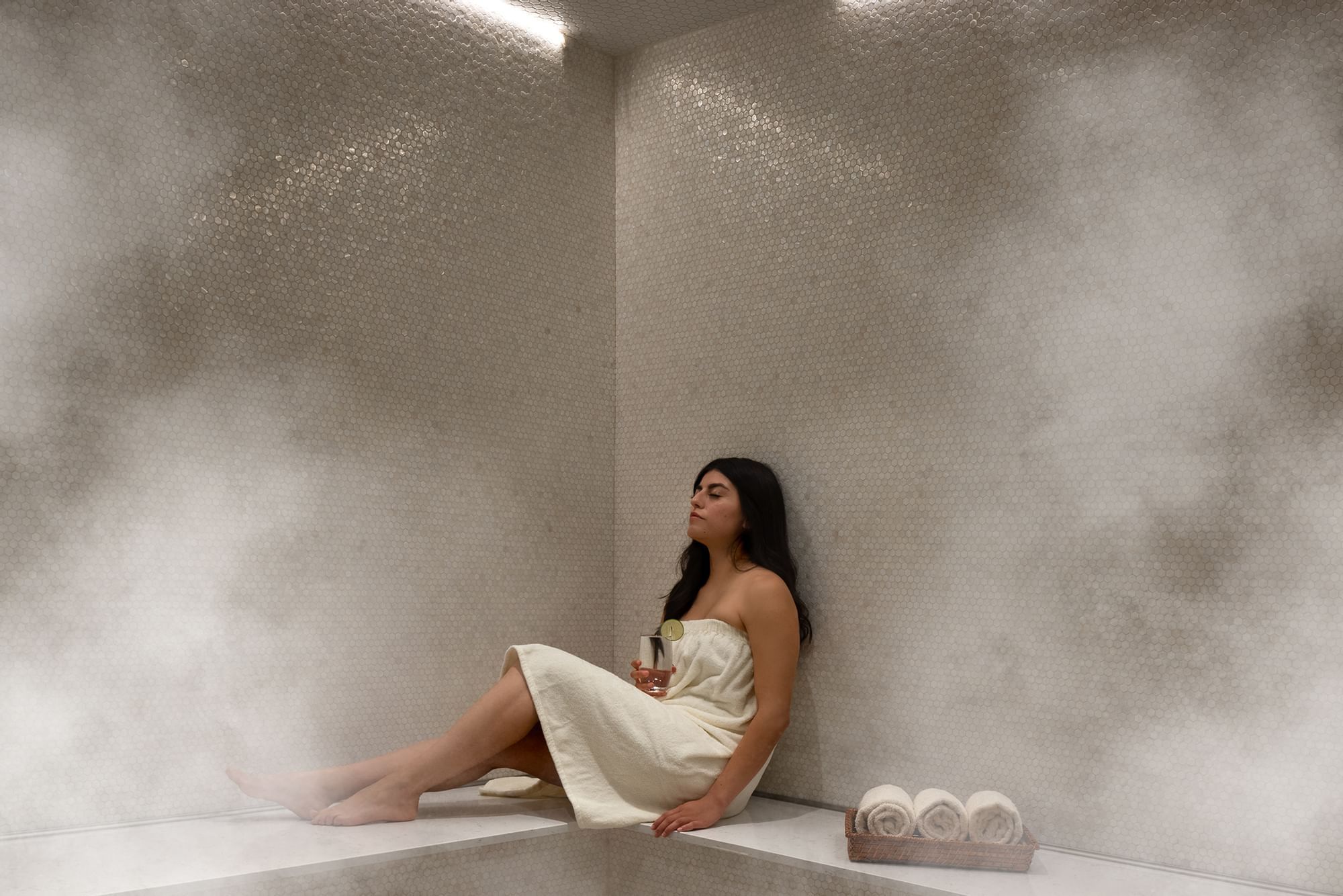 Woman sitting on a bench wrapped in a towel at Le Spa by Warwick Melrose