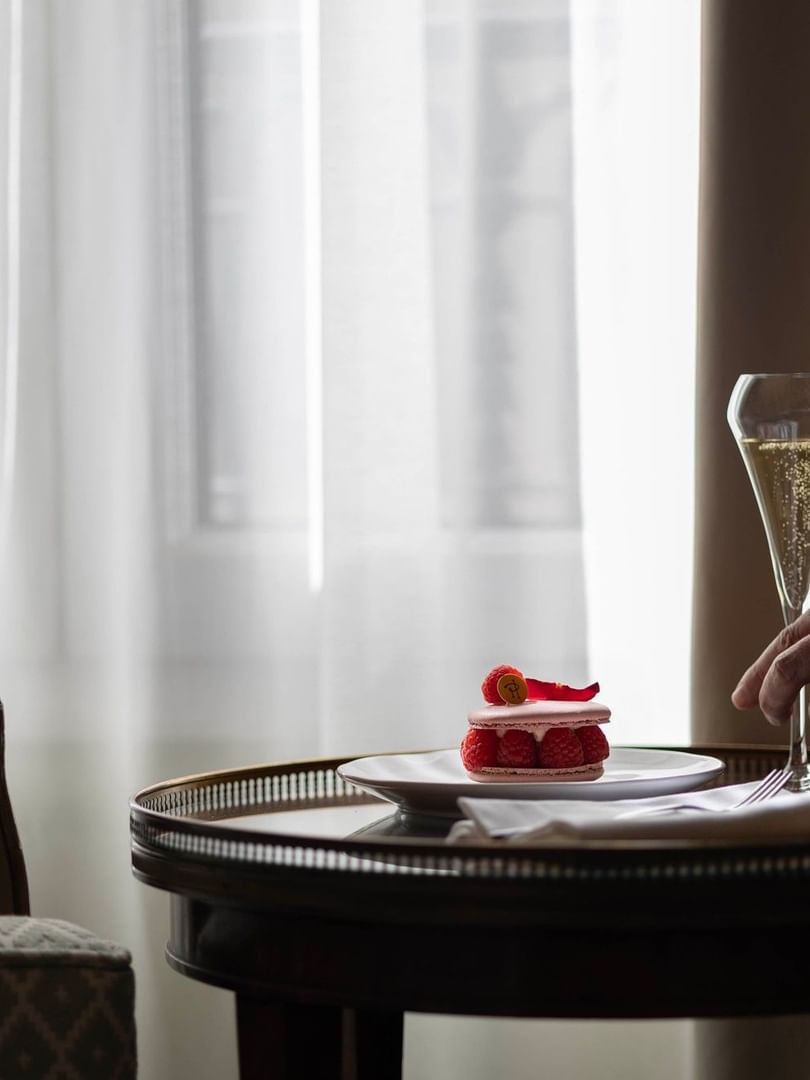 A hand places a champagne glass next to a raspberry dessert on a tray at Hôtel Westminster Paris.