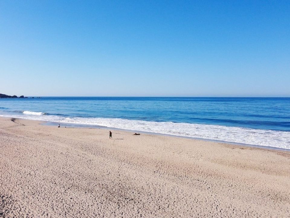 Personas caminando por una amplia playa de arena junto al océano cerca de Camino Real Hotels