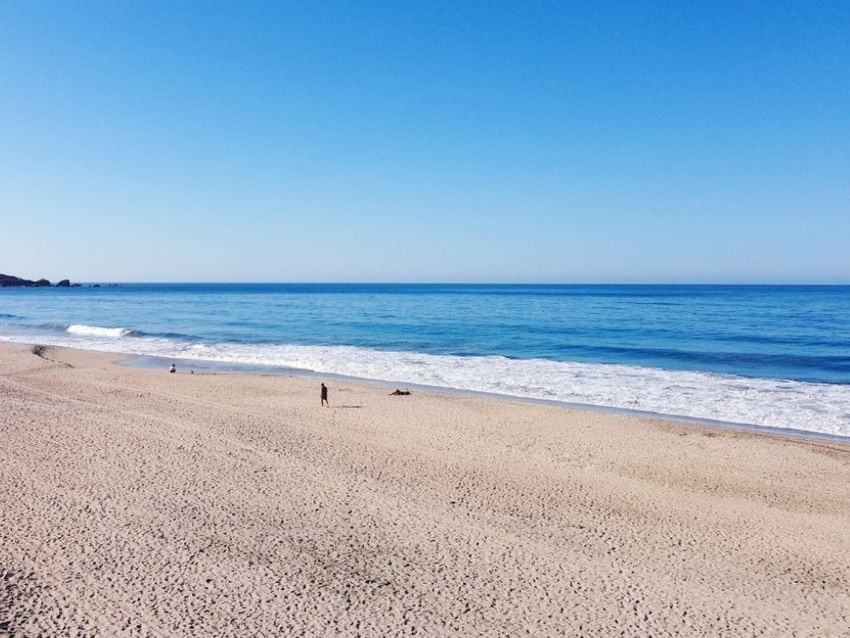 Personas caminando por una amplia playa de arena junto al océano cerca de Camino Real Hotels