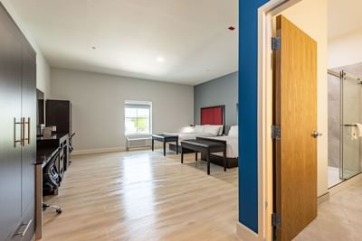 TV, work desk, and side cupboard facing the cozy beds in Dunedin hotel rooms with wooden floors at The J Hotel