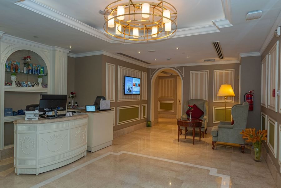 Plush armchairs by a round side table under a large gold chandelier in the wellness center at Warwick Doha Hotel