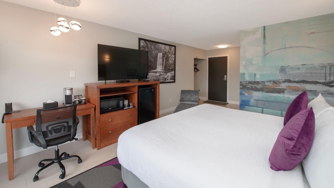 Modern hotel king room with a bed, desk, TV, and abstract art on the wall.