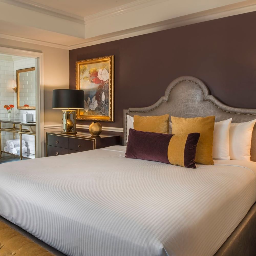 King bed with purple accent wall, and a view into a marble bathroom in Follie Suite at Warwick New York