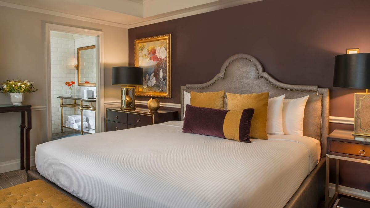 King bed with purple accent wall, and a view into a marble bathroom in Follie Suite at Warwick New York