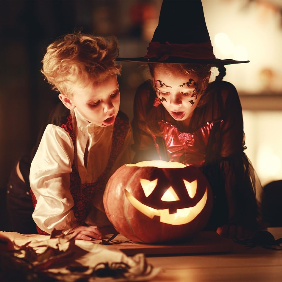 Bambini mascherati guardano una zucca di Halloween illuminata.