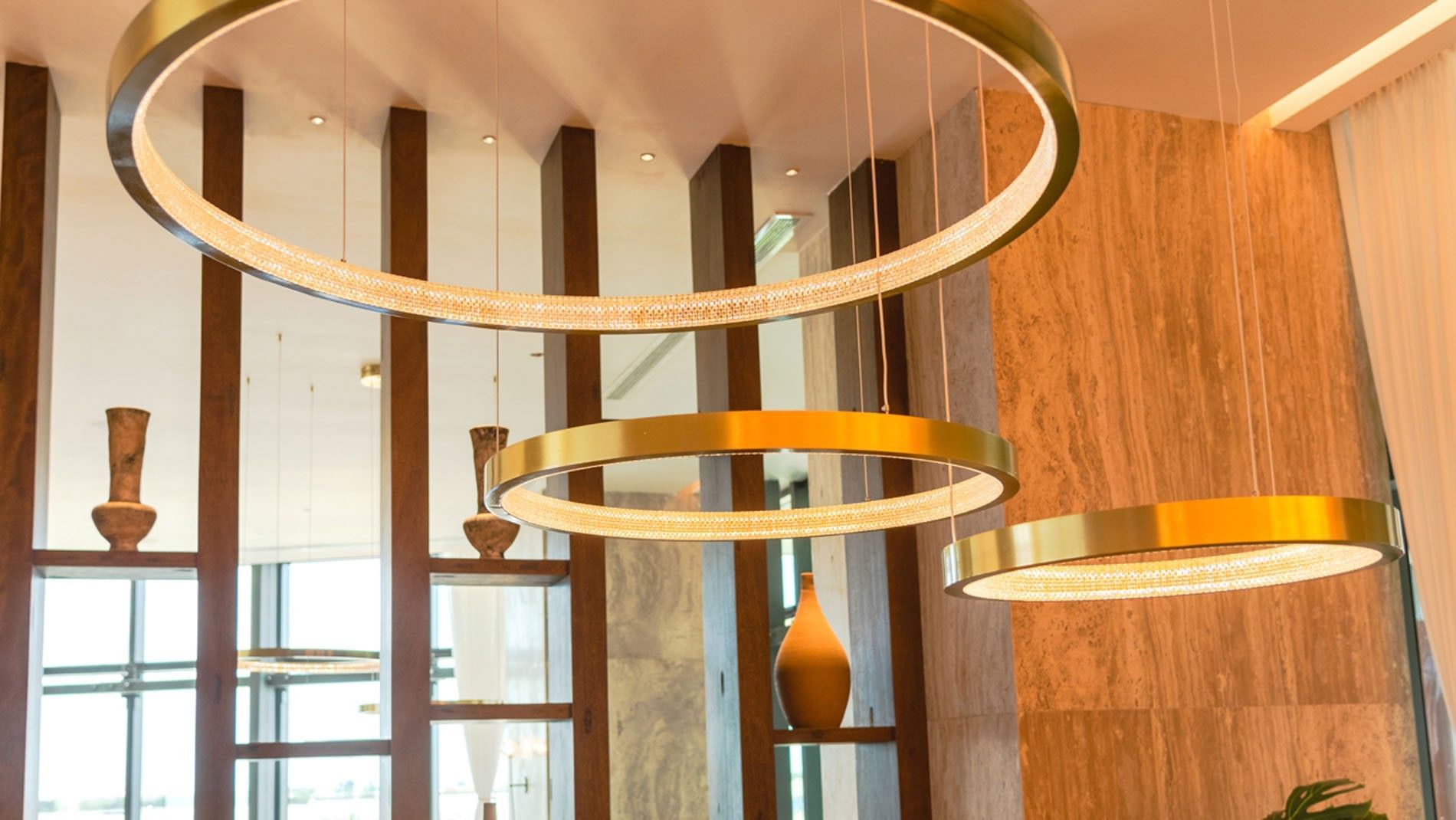 Luxury interior of La Huerta restaurant featuring modern circular gold chandeliers and wood accents at Camino Real Merida