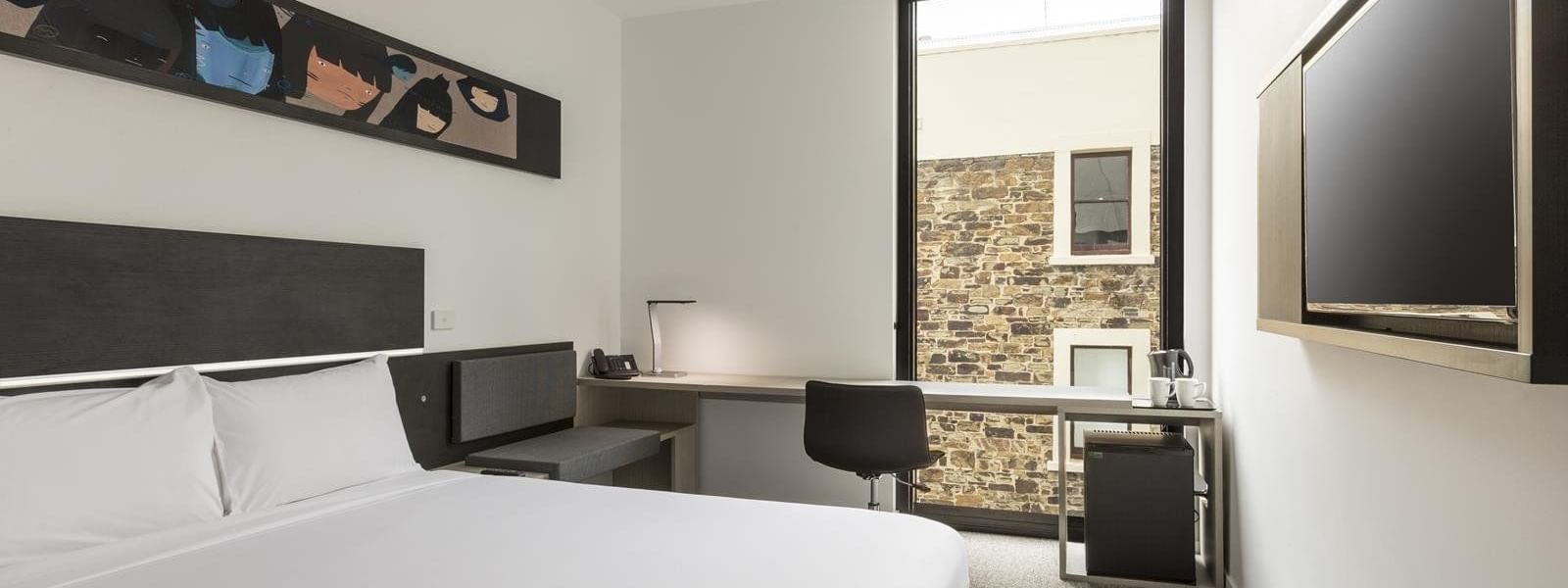 TV facing bed and workspace by the large window in Standard Room One Queen Bed at Ibis Adelaide
