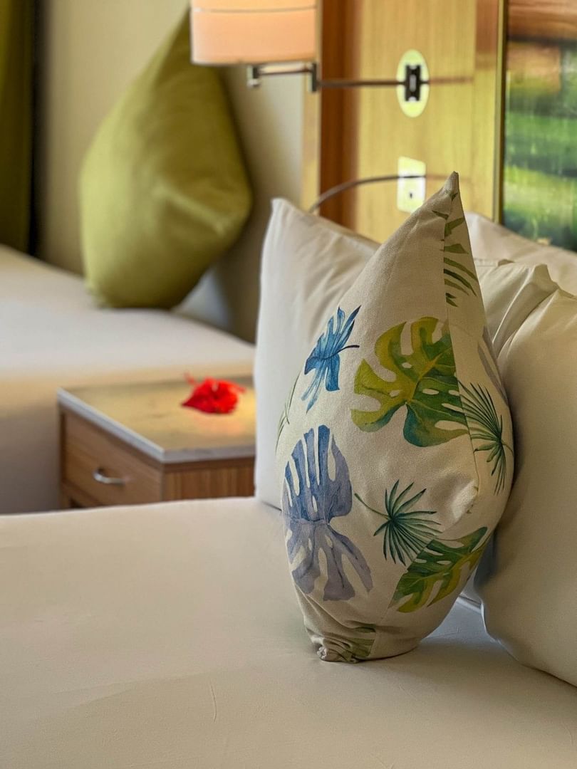 Tropical leaf pillow on a white bed by a wooden nightstand in Garden View Room at The Naviti Resort Korolevu, Fiji