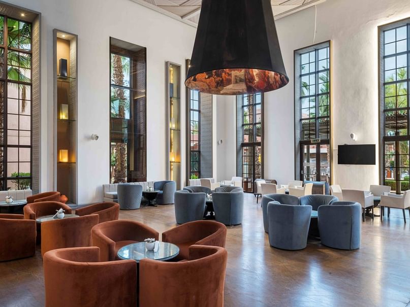 Elegant lounge with large windows, wooden floors, circular chairs, a round table, and a large ceiling lamp.