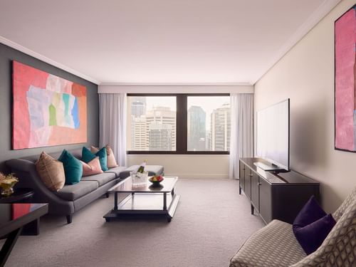 Living area with a gray couch, colorful wall art, and a city view in Signature Suite at Sofitel Brisbane Central
