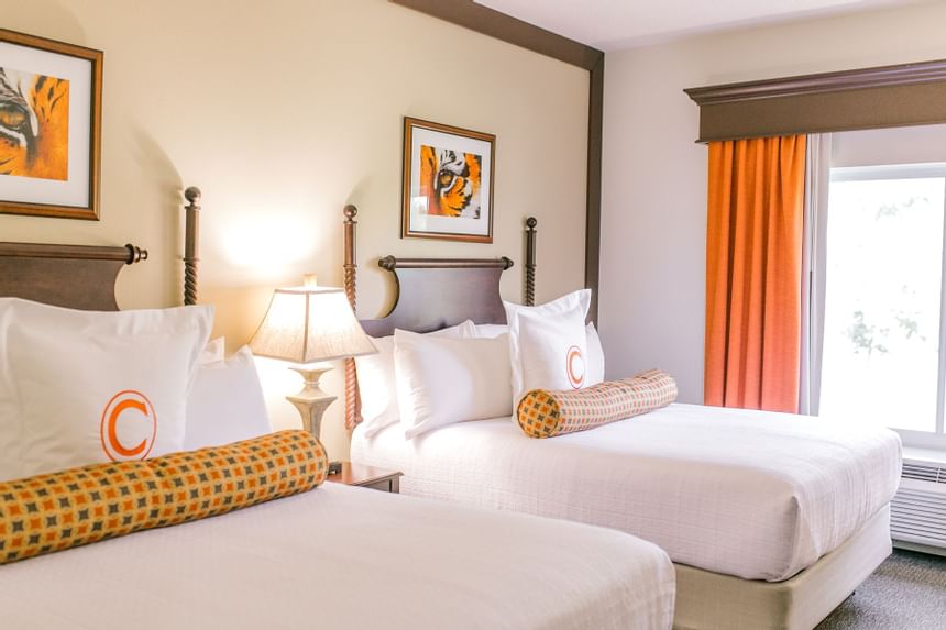 two double beds in hotel room with window and orange curtains