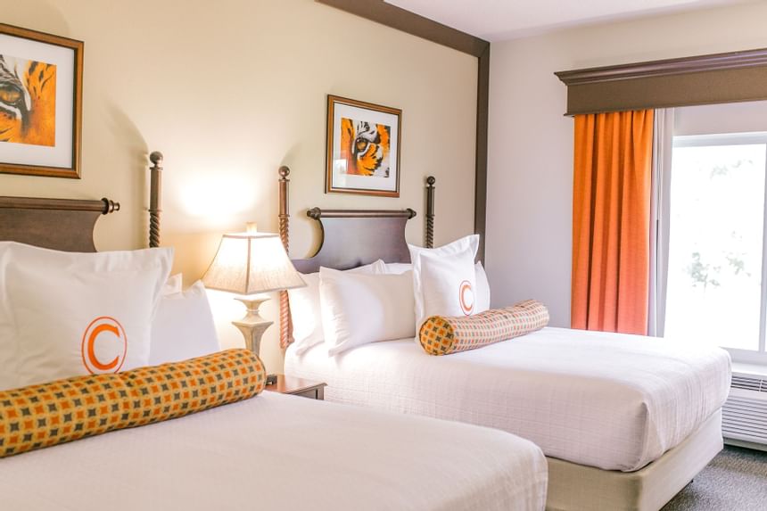 Two white beds by orange window curtain in the Double Executive Queen Lakeside at Clemson University Conference Center & Inn