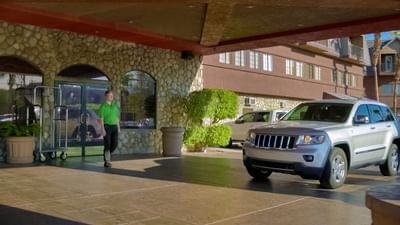 Staff member with luggage cart assisting guests under covered entrance with parked vehicle at London Bridge Resort