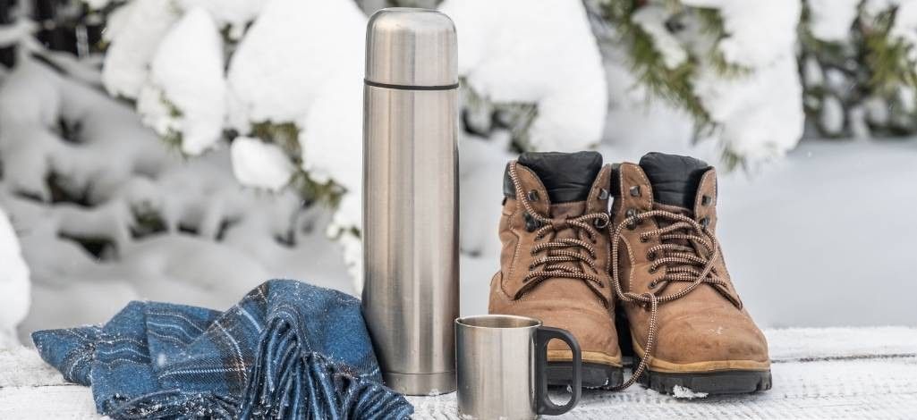 Winter boots and thermos in snowy setting
