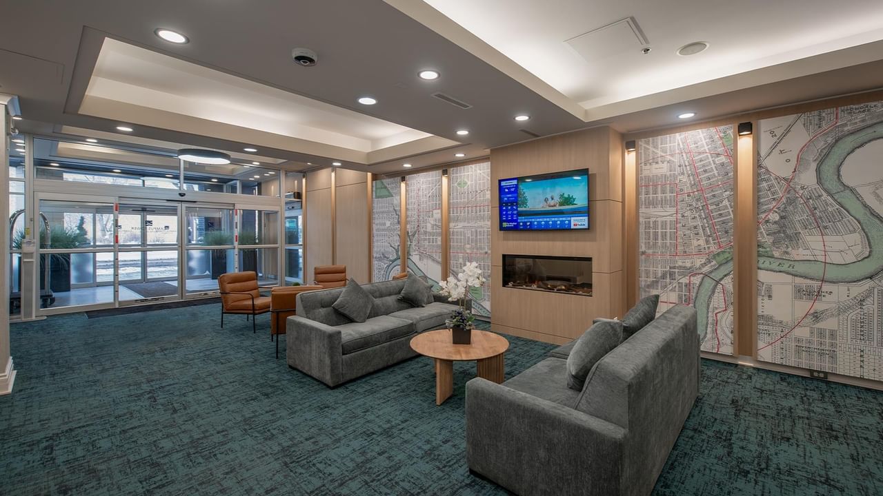 Hotel lobby with couches, coffee table, TV, and decorative wall maps.