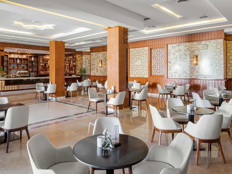 Elegantes Restaurant mit weißen Tischen und Stühlen, dekorierten Wänden und einer Bar im Hintergrund.