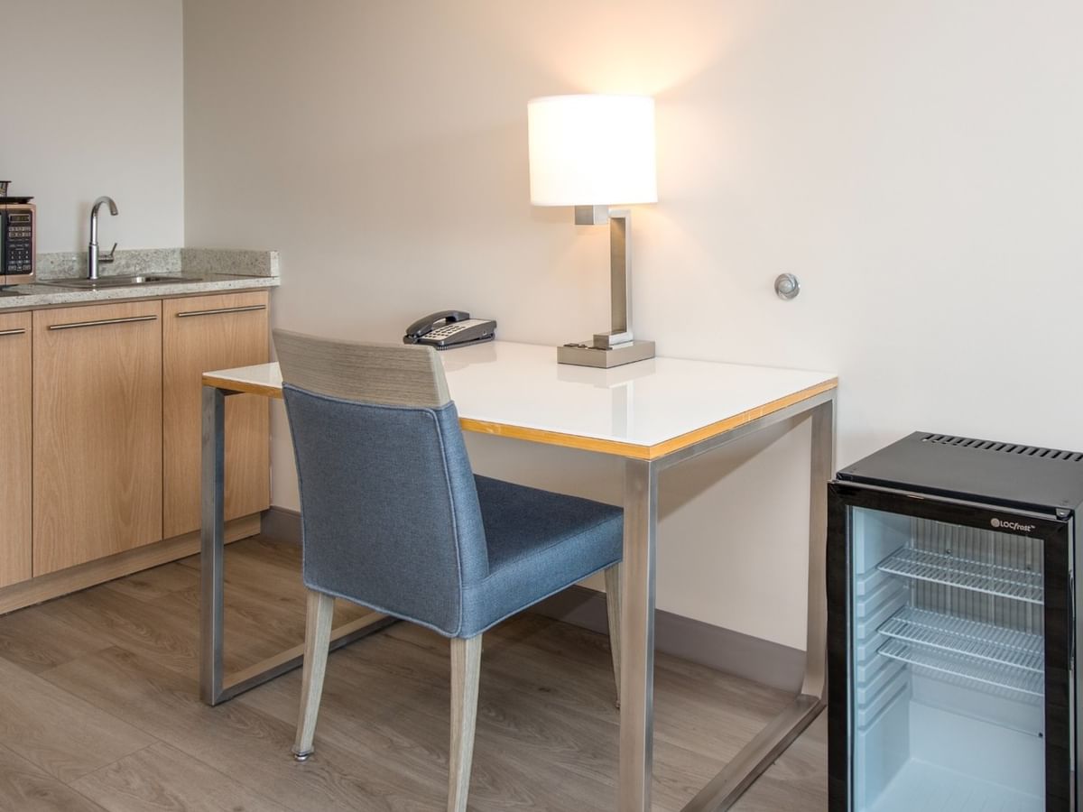 Hotel room with wooden cabinets, sink, coffee maker, microwave, table, chair, and small refrigerator.