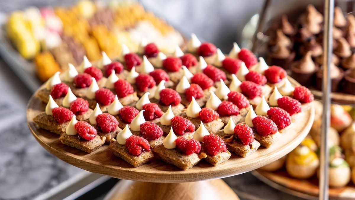 Wooden platter of desserts topped with cream swirls and fresh raspberries in Epicurean at Crown Towers Sydney