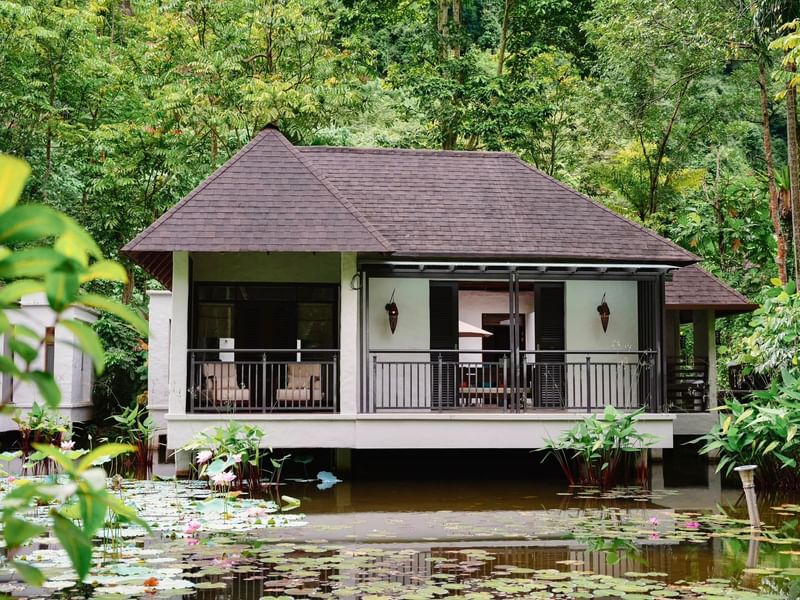 Water villa surrounded by lush greenery and a pond with lotus flowers at The Banjaran Hotsprings Retreat