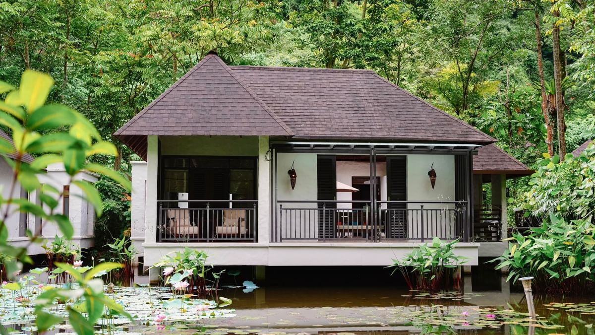 Water villa surrounded by lush greenery and a pond with lotus flowers at The Banjaran Hotsprings Retreat