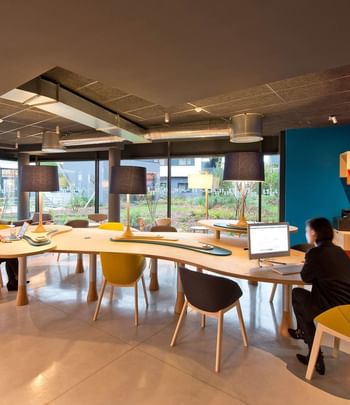 Business Corner arranged with a long table and chairs at Nomad Hotels Paris Roissy