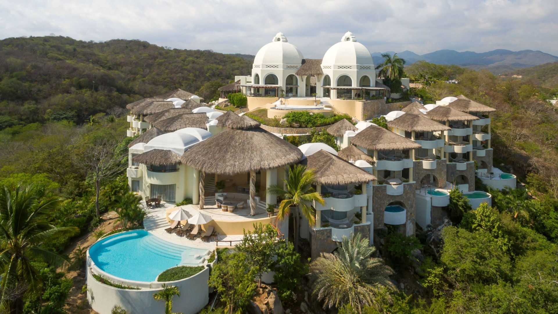 Stunning hillside resort at Quinta Real Huatulco, featuring thatched roofs and a bright blue pool