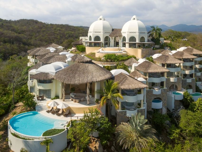 Aerial view of Quinta Real Huatulco featuring white domes by a pool surrounding thatched roofs at Tangolunda Bay