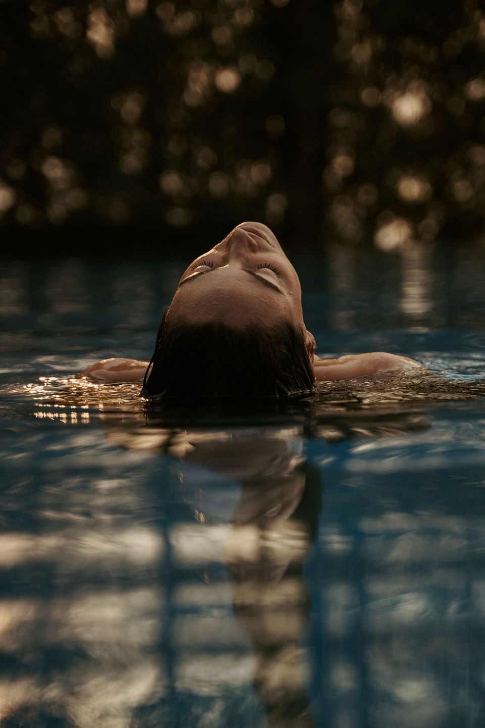 Woman floats in a pool, eyes closed, with soft light reflecting on the water's surface at The Dwarika’s Hotels and Resorts