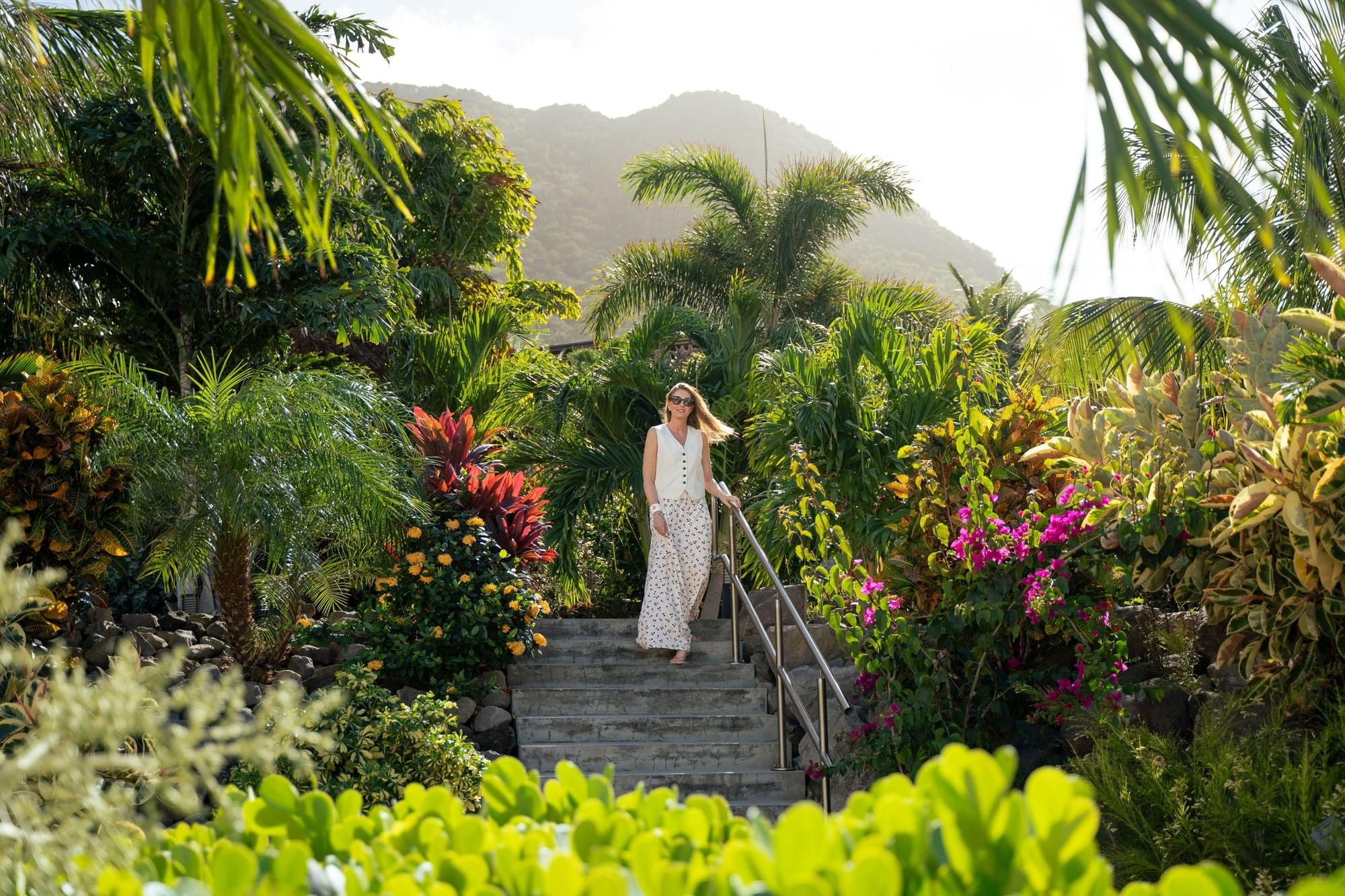 Woman walking down a stone staircase among vibrant tropical flowers and palm trees at Golden Rock Resort