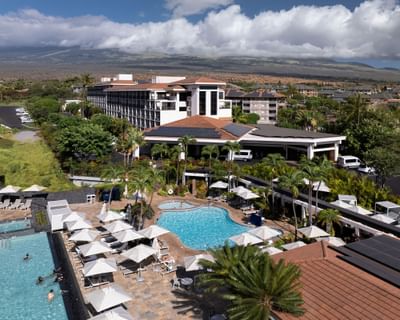 Aerial view of Maui Coast Hotel, highlighting the lounge chairs with umbrellas by the pool and mountains in the background