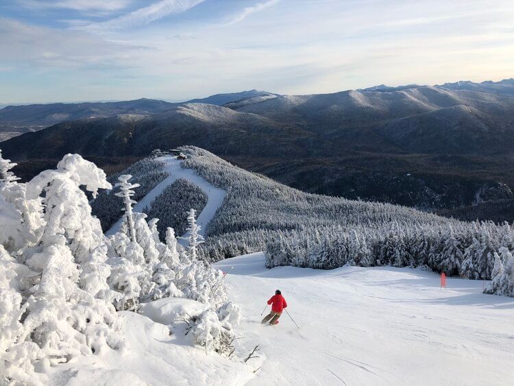 A skier in a red jacket carves down a snowy mountain slope with vast winter views near Lake Placid Club Grandview