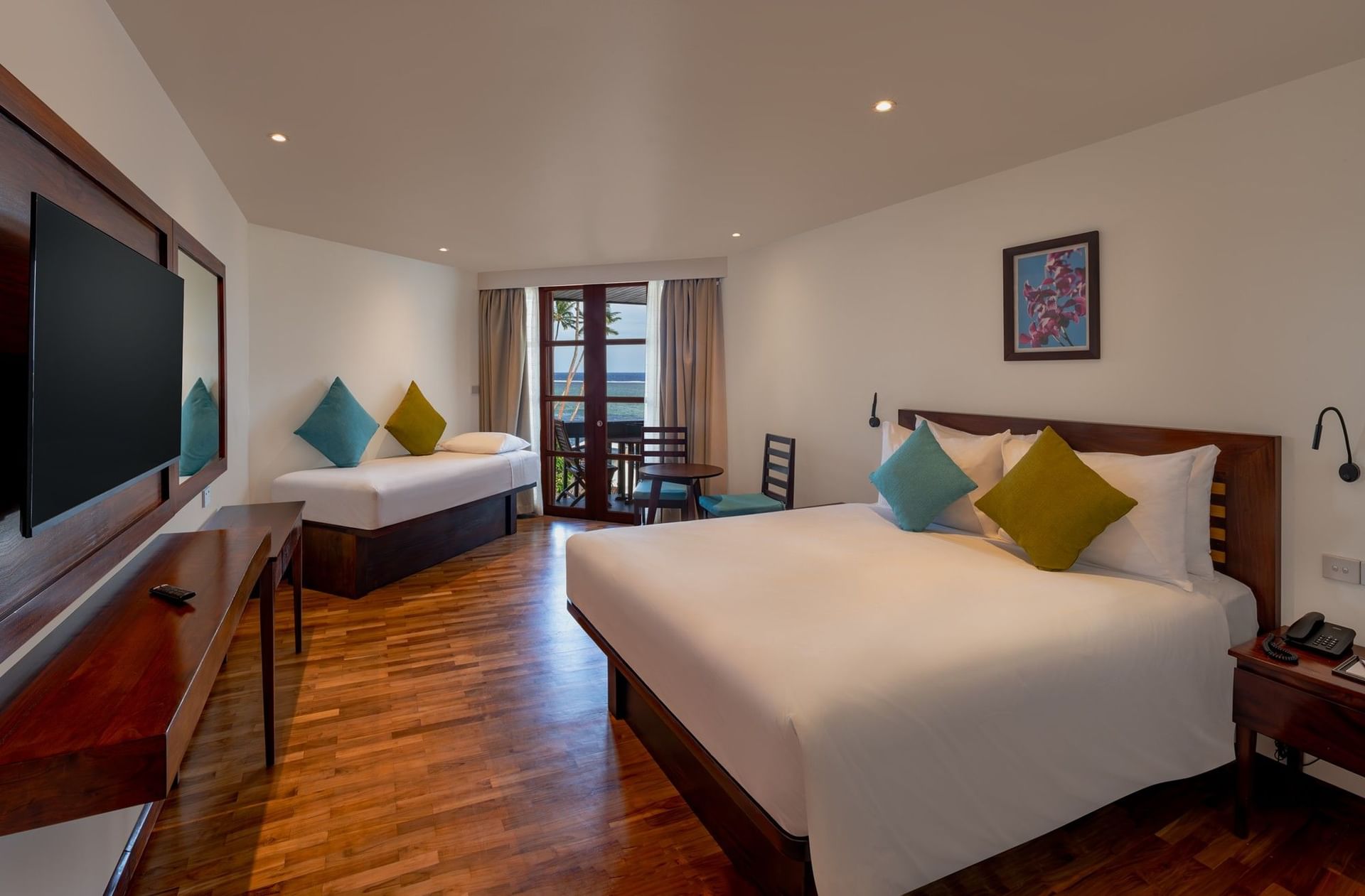 Plush bed by a wooden desk under soft lights with glass doors in Ocean View Rooms at Warwick Fiji Resort and Spa