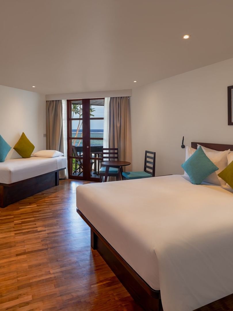 Plush bed by a wooden desk under soft lights with glass doors in Ocean View Rooms at Warwick Fiji Resort and Spa