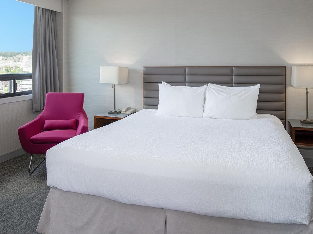 King bed with white linens, pink accent chair, city views, and modern furnishings at Coast Prince George Hotel.
