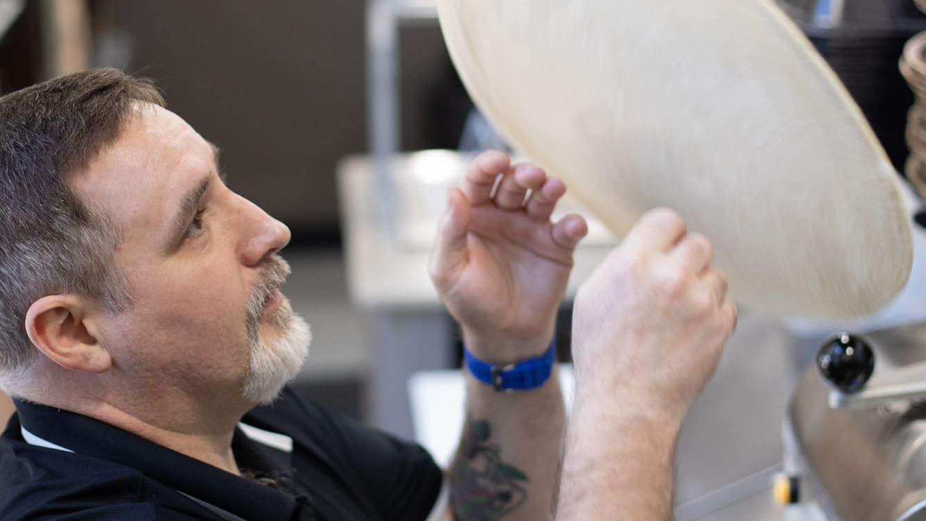 Man is skillfully shaping a pizza dough in Bruno’s Pizza at Watersound Inn