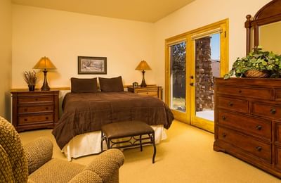 A spacious bedroom with a queen bed, wooden furniture, and a glass door leading outside at The Stanley Hotel
