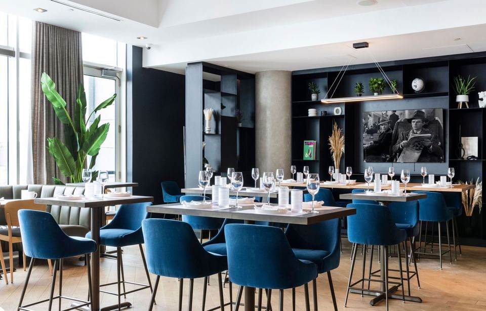 Roses social dining area with blue velvet chairs and small wooden tables facing bar area at Hotel X Toronto