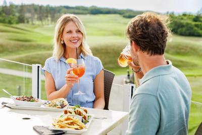 Couple enjoying drinks and lunch on an outdoor patio overlooking the golf course at Rodd Crowbush Golf & Beach Resort