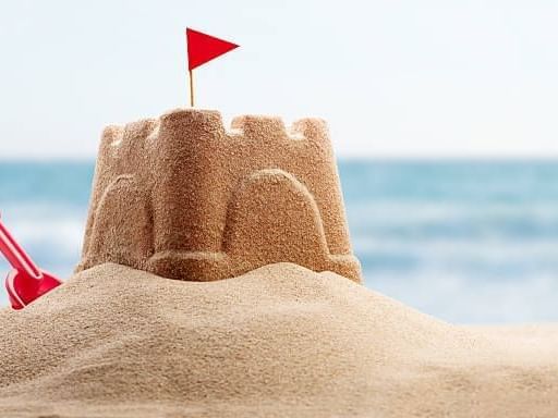Primer plano de una pala de juguete roja junto a un castillo de arena con una bandera, en la playa cerca de Las Casitas Village.