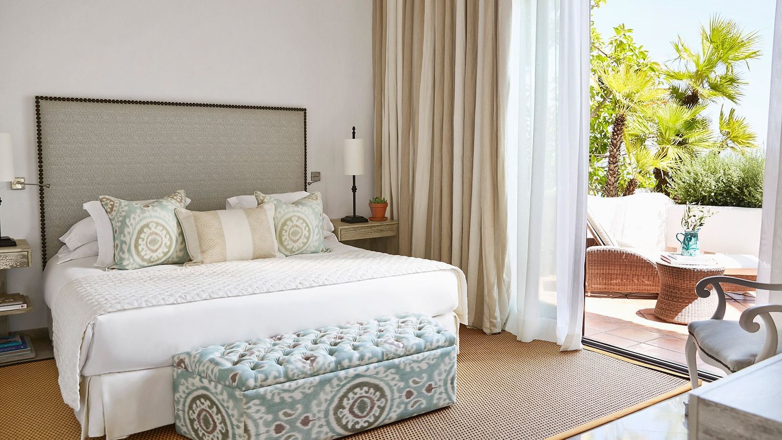 Royal Beach Suite with a king bed, a studded gray headboard, a patterned tufted bench, & patio access at Marbella Club