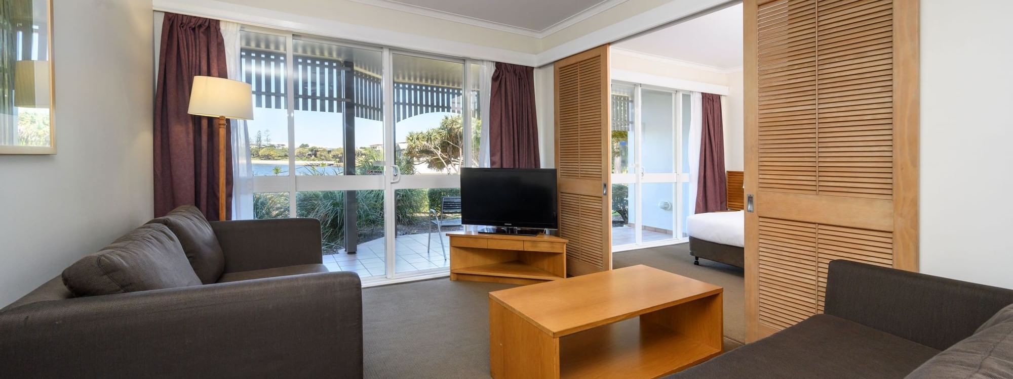 TV lounge with plush seating by the window and carpet floors in One & Two-Bedroom Suites at Novotel Sunshine Coast Resort
