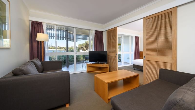 TV lounge with plush seating by the window and carpet floors in One & Two-Bedroom Suites at Novotel Sunshine Coast Resort