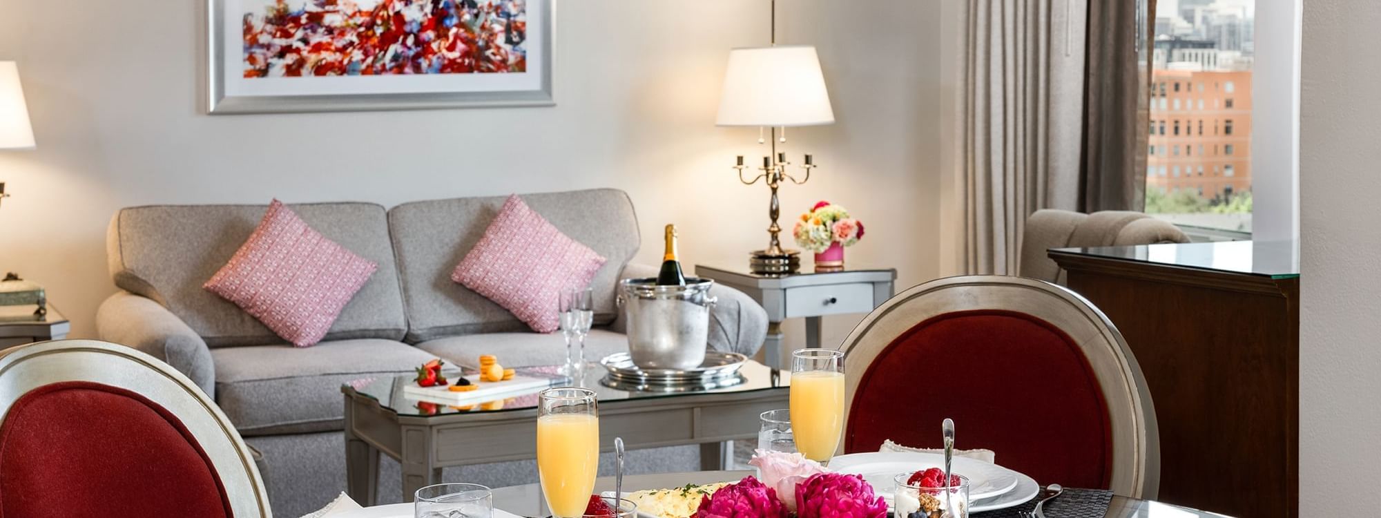Dining area set with a gourmet breakfast, flowers, and a champagne bucket in suite at Warwick Melrose Dallas