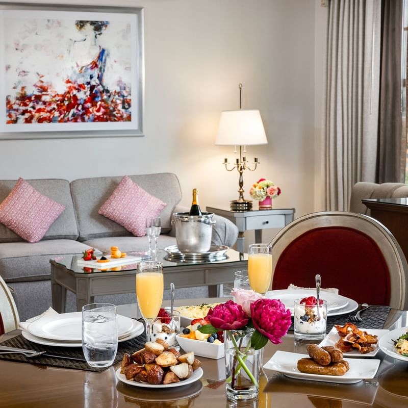 Dining area set with a gourmet breakfast, flowers, and a champagne bucket in suite at Warwick Melrose Dallas